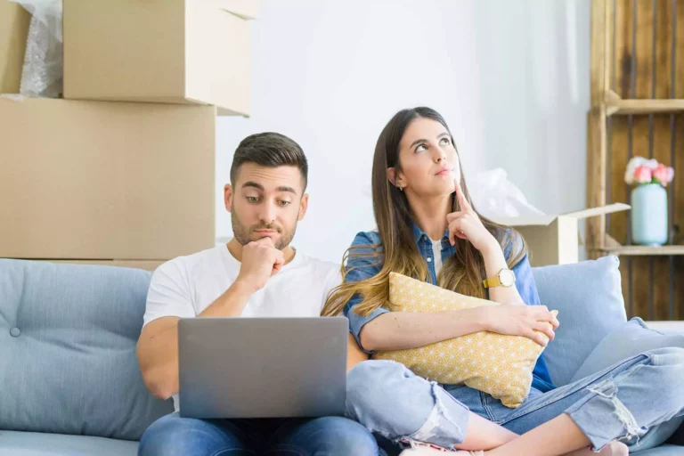 Junges Paar sitzt auf der Couch und fragt sich, was es beim Immobilienkauf beachten muss